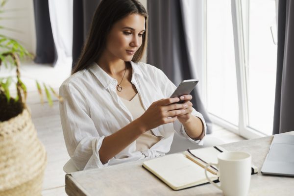 Attractive business woman sits at table in front of laptop and talks on mobile phone, negotiates on the phone. Attractive business woman sits at table in front of laptop and talks on mobile phone, negotiates on the phone. Beautiful brunette girl uses gadgets for work. Online training, remote work from home
